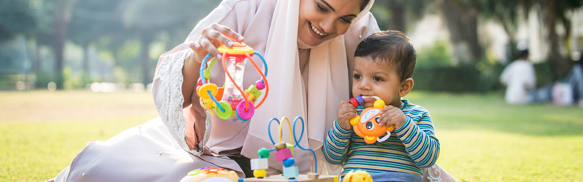 Mother in hijab with infant, playing with toys in the park